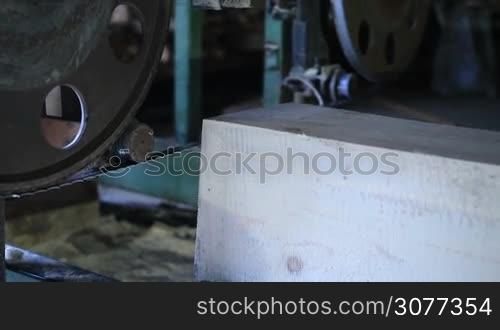 The process of cutting timber into planks for construction with bandsaw at sawmill. Pine wood trimming with band saw in workshop