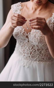 The process of equipping the bride before the wedding.. The bride in an openwork dress holds a necklace in her hands 3795.