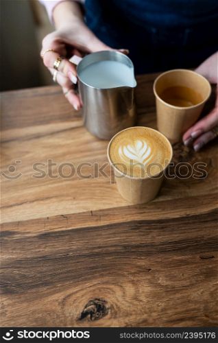 The process of making a barista cappuccino with a beautiful pattern on the foam in an eco-craft glass. Coffee to go concept. The process of making a barista cappuccino with a beautiful pattern on the foam in an eco-craft glass. Coffee to go concept.