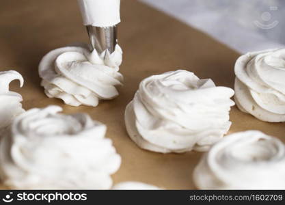 The process of making marshmallow. Close up hands of the chef with confectionery bag cream to parchment paper at pastry shop kitchen