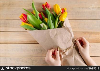 The process of wrapping bouquet of fresh tulips in eco-friendly craft paper. Step 3. Gift for spring holiday. Flower business.. The process of wrapping bouquet of fresh tulips in eco-friendly craft paper. Step 3.