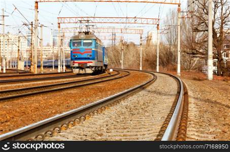 The prospect of a multi-channel railway for electric trains with overhead power lines in the early spring morning, against the backdrop of an urban blurred landscape.. Multichannel railway tracks with a turn for the passage of electric trains.