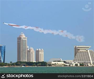 The Qatar Emiri Air Force gives a National Day flying display over Doha Bay, and the high-rise district. Maroon and white are the colours of the Qatari flag