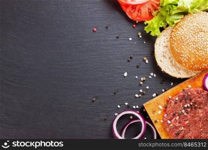 The raw ingredients for the homemade burger on black slate background. Top view, flat lay with copy space for text.. The ingredients for the burger