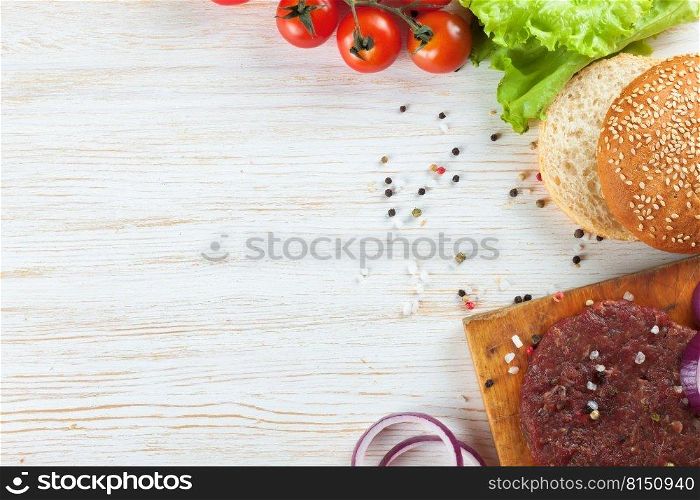 The raw ingredients for the homemade burger on white wooden background. Beef cutlet, tomato, salad, onion, wheat bun, spice. Top view, flat lay, mockup with copy space for text. The ingredients for the burger on white wooden background