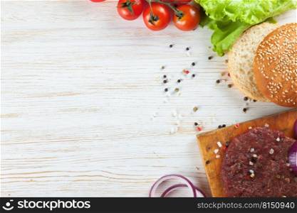 The raw ingredients for the homemade burger on white wooden background. Beef cutlet, tomato, salad, onion, wheat bun, spice. Top view, flat lay, mockup with copy space for text. The ingredients for the burger on white wooden background