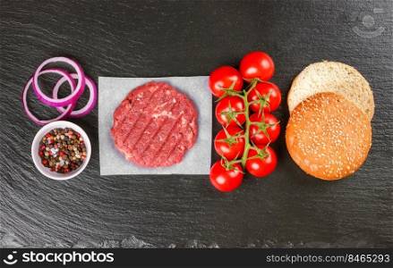 The raw ingredients for the homemade burger. Raw coutlet, tomatoes, cheese, salad, spices, onion, wheat bun on black slate background. Top view. Flat lay.. The raw ingredients for the homemade burger on black slate background. Top view.
