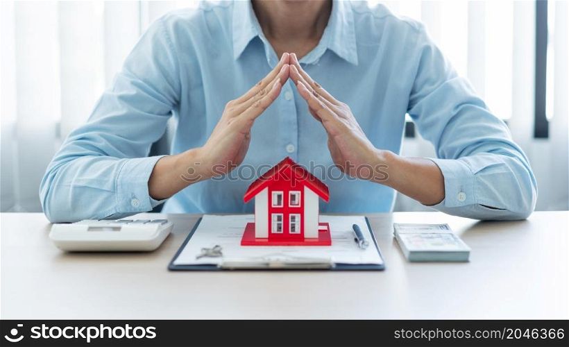 The real estate concept the realtor presenting his work towards his customer by putting the red house model in front of him, raising his hands and putting his hand together.