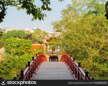 The Red Bridge in public park garden with trees and reflection in the middle of Hoan Kiem Lake in Downtown Hanoi. Urban city at sunset, Vietnam. Cityscape background.