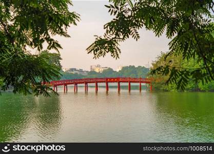 The Red Bridge in public park garden with trees and reflection in the middle of Hoan Kiem Lake in Downtown Hanoi. Urban city at sunset, Vietnam. Cityscape background.