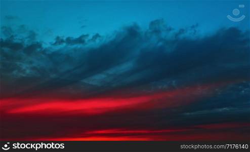 The red glow before dawn on a dark dramatic cloudy sky - an amazing colorful contrasting heavenly background with space for copy.