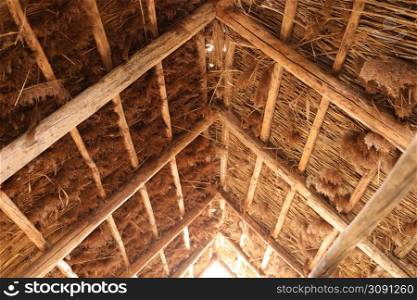 The reed roof on the house. Natural building materials.Texture of old thatched roof from the inside. Old technology. Wooden house architecture. The reed roof on the house. Natural building materials.Texture of old thatched roof from the inside. Old technology. Wooden house architecture.