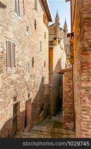 The renaissance town of Urbino, Marche, Italy. A view of the Ducale Palace (Palazzo Ducale) seen from a narrow street in Urbino city, Marche, Italy