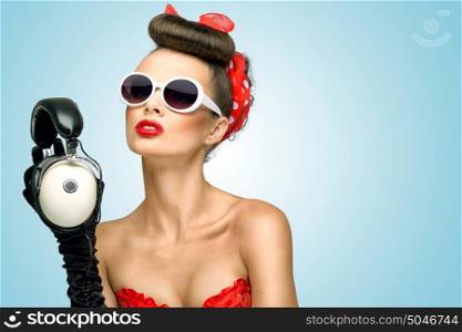 The retro photo of a cute pin-up girl in sunglasses with vintage music headphones.