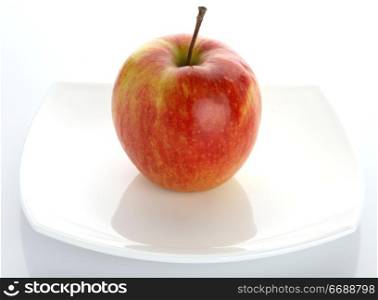The ripe red apple lays on a white plateThe ripe red apple lays on a white plate