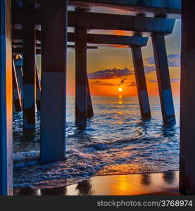 The rising sun peeks through clouds and is reflected in waves by the Nags Head fishing pier on the outer banks of North Carolina