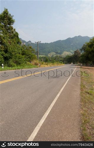 The road on the mountains. The road cuts through the mountains. The trees along the road