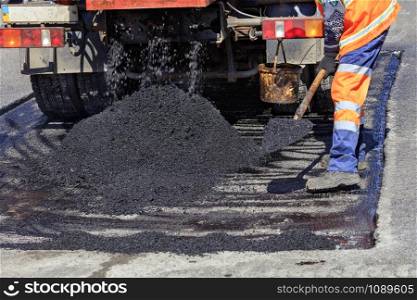 The road service worker shovel new asphalt during construction and patching of the road.. Road worker distributes a piece of asphalt with a shovel for patching of the road