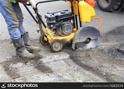 The road technician starts the engine of a gasoline diamond saw to remove old asphalt during repairs on the roadway.. The worker starts the engine of the gasoline cutter to cut and clear bad asphalt on the roadway.