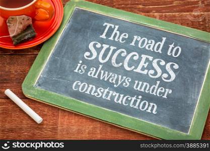 The road to success is always under construction - motivational text on a slate blackboard with chalk and cup of tea
