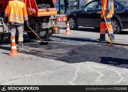 The road workers? team updates part of the road with fresh asphalt using shovels it to repair a small section of the road, image with copy space.. The group of road workers is repairing a section of the carriageway with fresh asphalt.