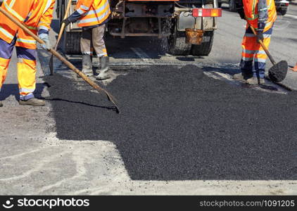 The road workers? working group updates part of the road with fresh hot asphalt and smoothes it for repair.. The working team smoothes hot asphalt with shovels by hand when repairing the road.