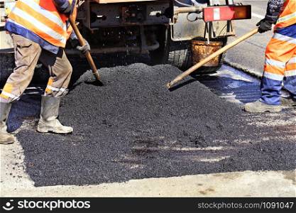 The road workers? working group updates the part of the road with fresh hot asphalt with shovels and distributes it evenly over the surface.. The working crew evenly distributes hot asphalt with shovels manually on the repaired site of the road.