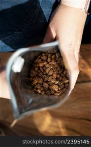 The roasted coffee bean is packaged in a bag that the barista holds in his hands. Top view, coffee preparation concept. The roasted coffee bean is packaged in a bag that the barista holds in his hands. Top view, coffee preparation concept.
