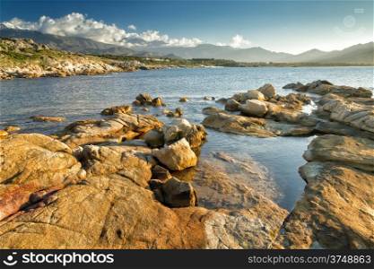 The rocks at Arinella Plage near Lumio in the Balagne region of Corsica with snow capped mountains in the distance