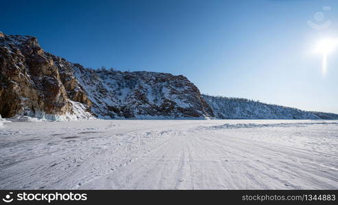 The rocky mountains are covered with snow. The blue color of the sky contrasts with the brown color of mountains and ground. Beautiful scenery of mountains, lake and skies. Lake Baikal, Russia.