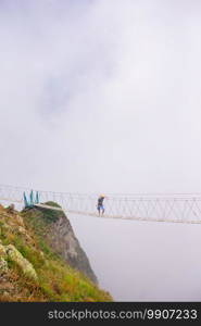 The rope bridge on the top of mountain of Rosa Khutor, Russia. Young guy on a pendant bridge over an abyss in the mountains. The rope bridge on the top of mountain of Rosa Khutor, Russia