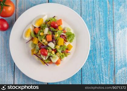 The salad is on a white plate, with a sandwich and tomatoes on the blue wooden floor.