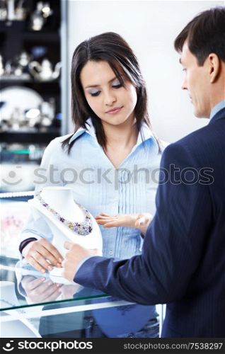 The saleswoman shows a necklace to the man in shop