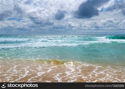 The sandy beach of the tropical ocean and the overcast sky with dramatic clouds.
