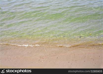 The sandy seashore with coming wave of green water..