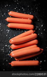 The sausages boiled on the table are in a row. On a black background. High quality photo. The sausages boiled on the table are in a row.