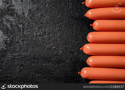 The sausages boiled on the table are in a row. On a black background. High quality photo. The sausages boiled on the table are in a row.