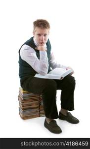 The schoolboy in a school uniform sits on a pack of books, with the opened book in hands