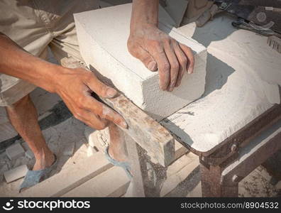 The sculptor&rsquo;s hands, which process a block of white stone on the desktop with tools. Hand Detail