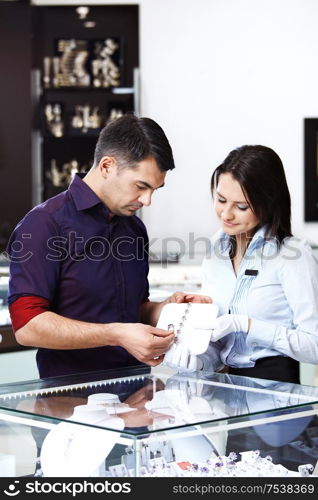 The seller in shop helps the man to pick up a jewel