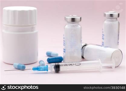 The set of medicine bottles, blue pills and injection syringe on pink background