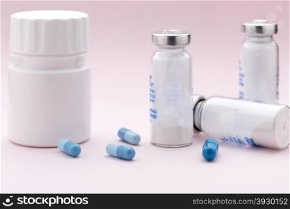 The set of medicine bottles, colorful capsules and injection syringe on pink background