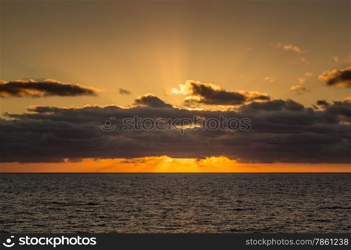 The seting sun goes down behind distant clouds over the mediterranean sea