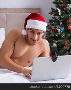 The sexy man in the bed wearing santa hat in christmas concept. Sexy man in the bed wearing santa hat in christmas concept