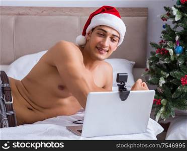 The sexy man in the bed wearing santa hat in christmas concept. Sexy man in the bed wearing santa hat in christmas concept