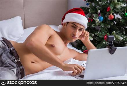 The sexy man in the bed wearing santa hat in christmas concept. Sexy man in the bed wearing santa hat in christmas concept