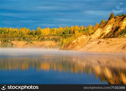 The shore of the misty lake in the early morning lit by the bright sun . Autumn landscape.Vsevolozhsk, Leningrad region.. The shore of the misty lake in the early morning lit by the bright sun . Autumn landscape.