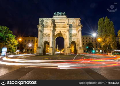 The Siegestor Victory Arch in Munich at dusk with traffic going around the arch.