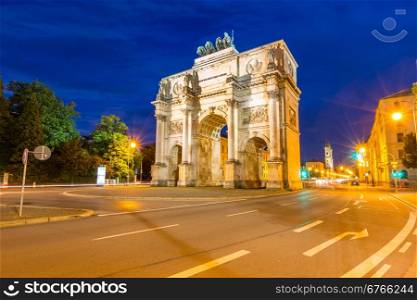 The Siegestor Victory Arch in Munich at dusk with traffic going around the arch.