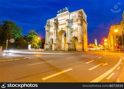 The Siegestor Victory Arch in Munich at dusk with traffic going around the arch.